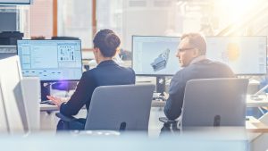 サンフレアで明るい晴れのオフィスでデスクトップコンピュータに取り組む技術エンジニアのチームのバックビュー